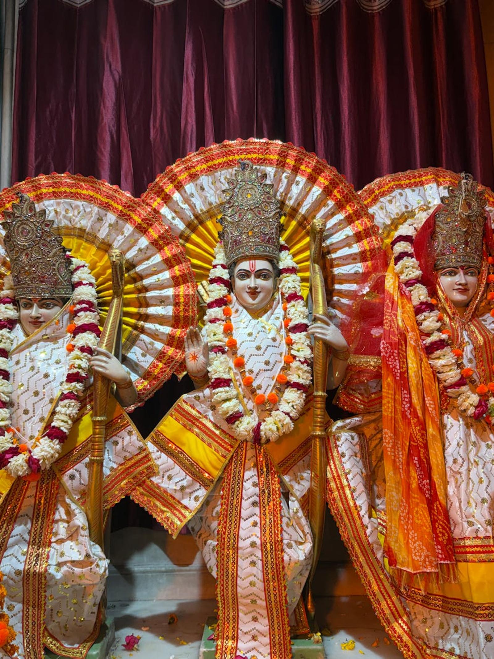 Three temple idols dressed in white and gold with floral garlands on stage