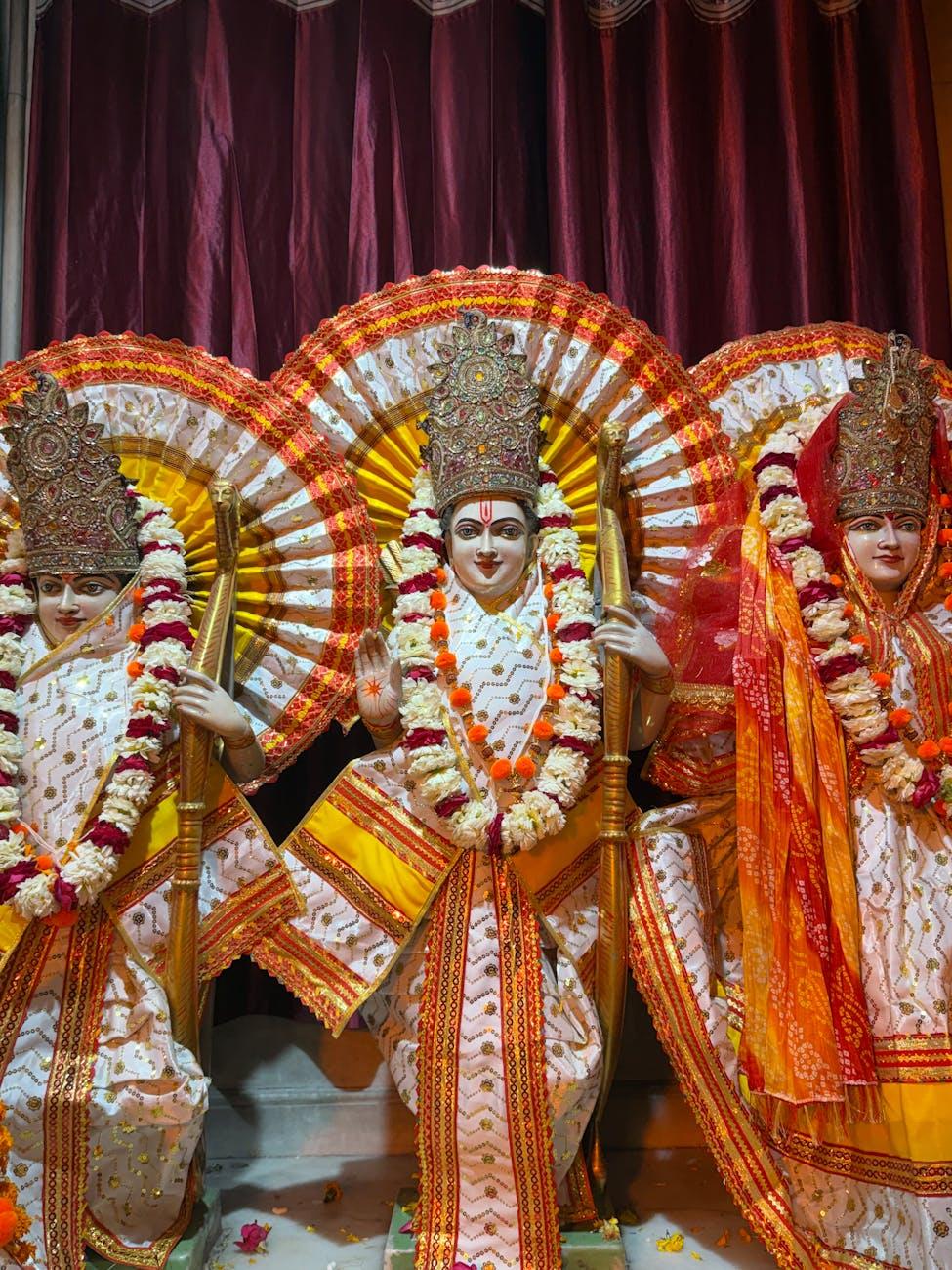 Three temple idols dressed in white and gold with floral garlands on stage
