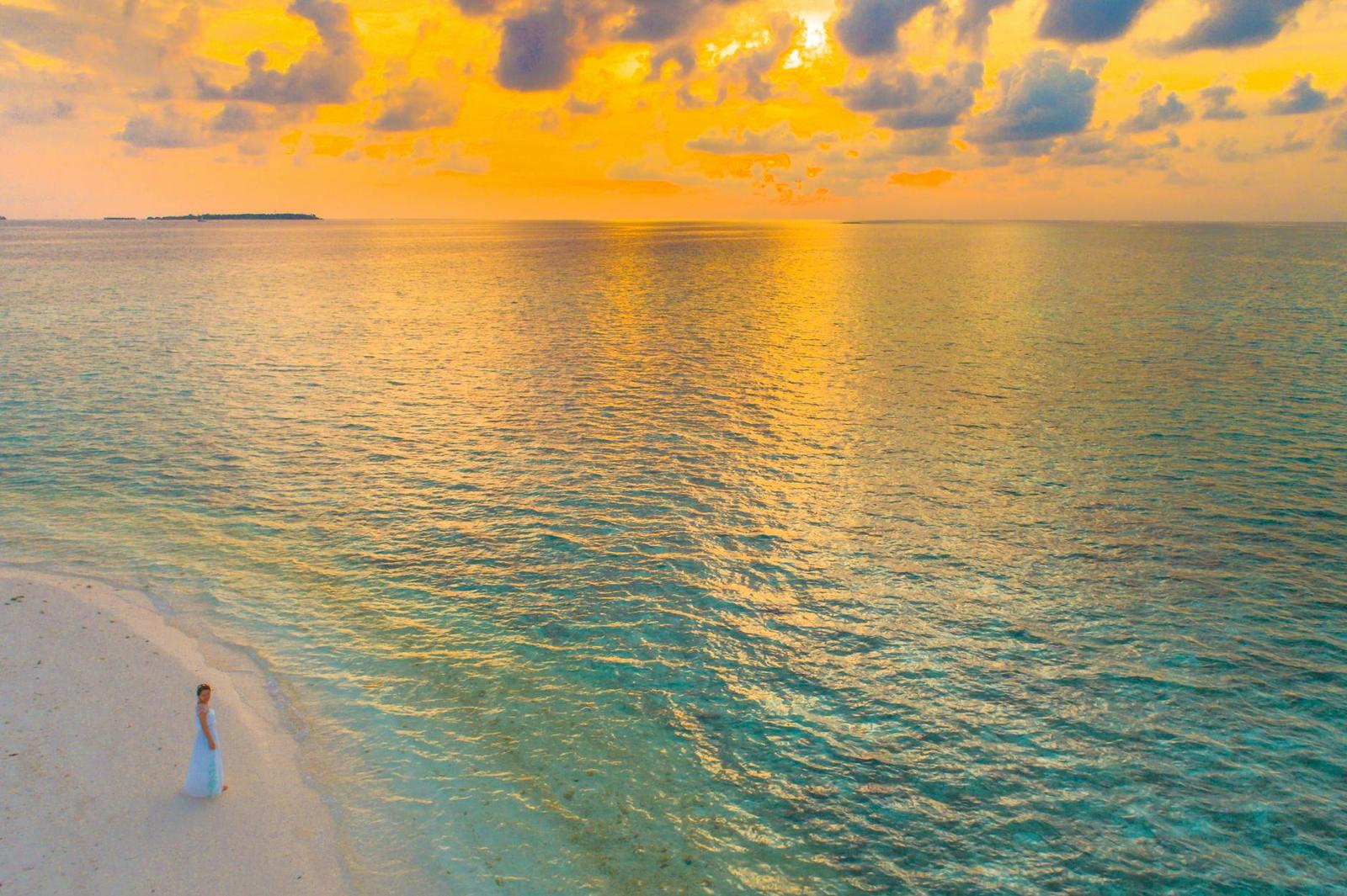 A lone figure in white walking a sandbar at sunset