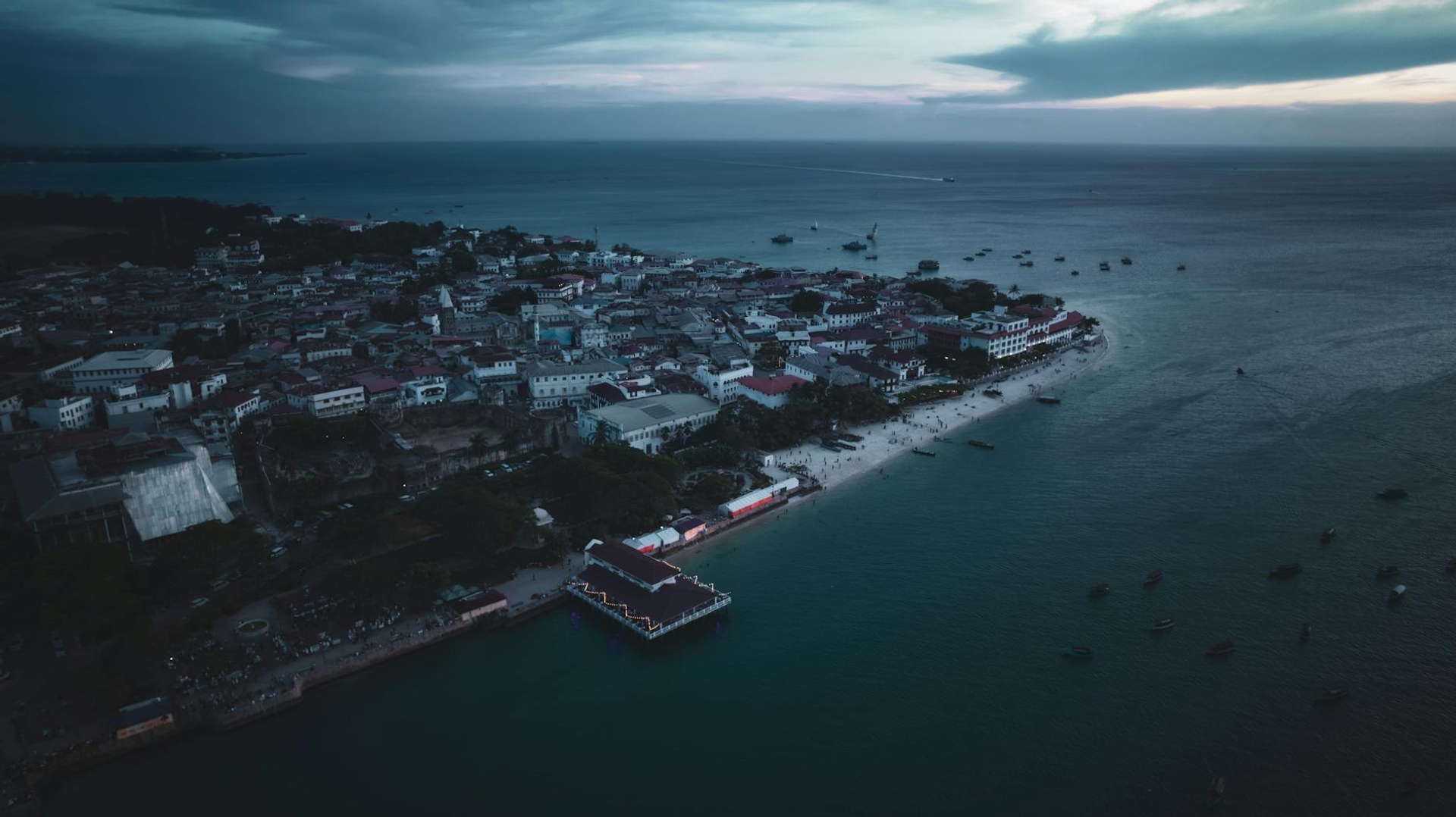 Aerial dusk view of a coastal town with a jetty extending into calm water