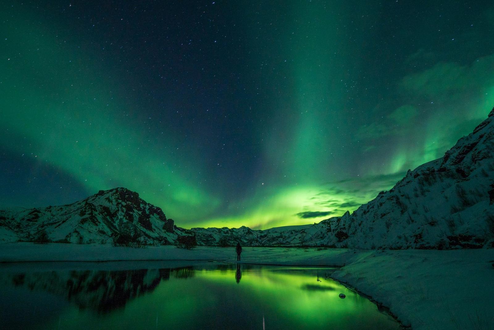 The northern lights swirling above snow-capped mountains and a still lake
