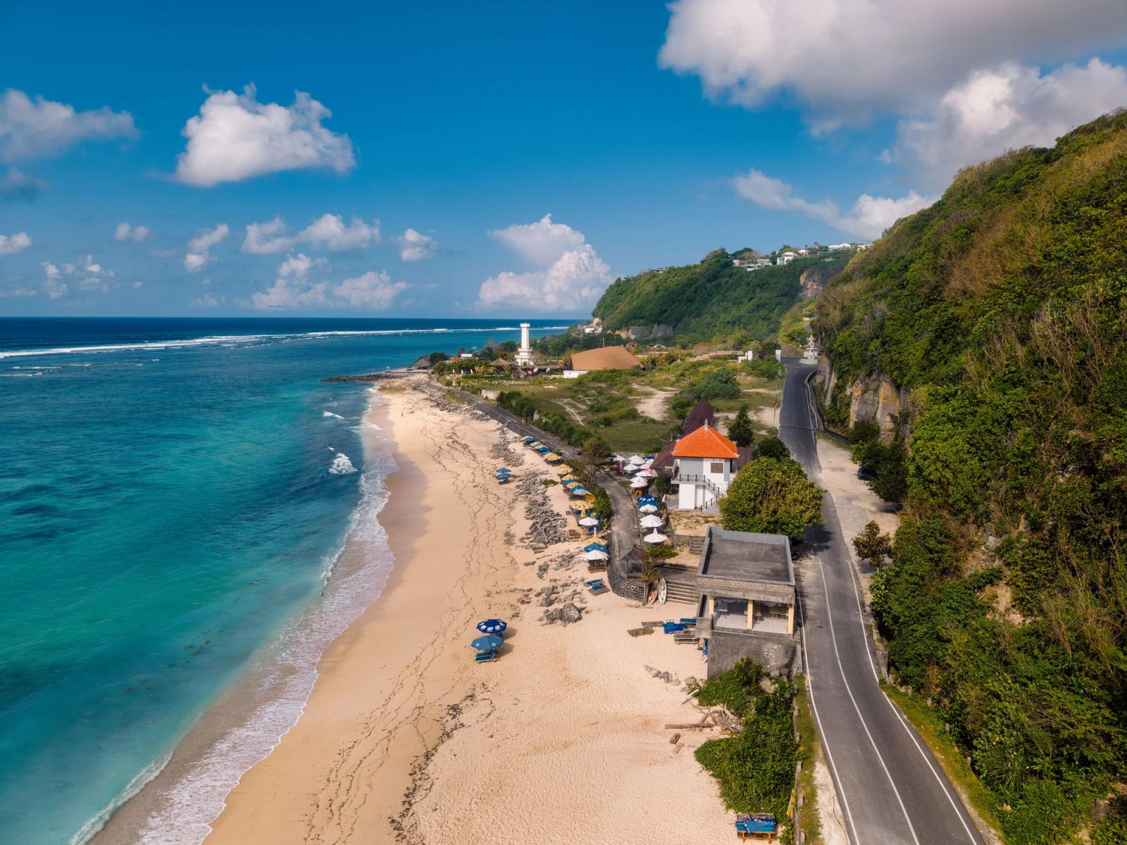 Aerial view of a beachfront road winding past a lighthouse and cafe