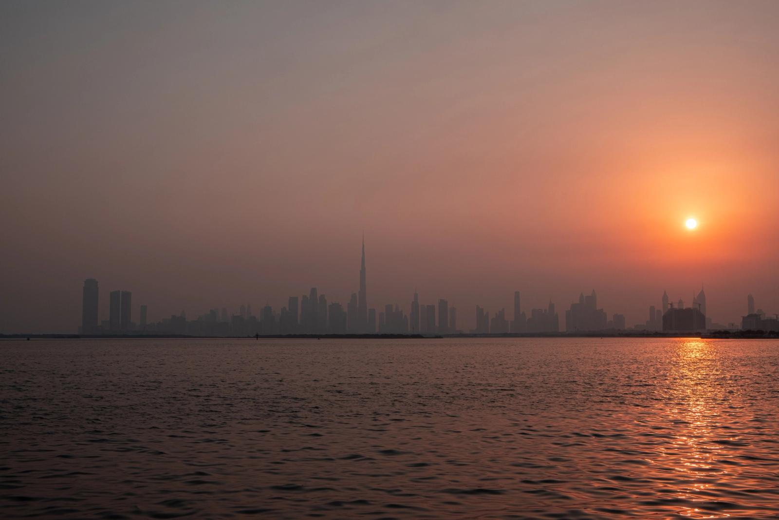 Serene view of Dubai skyline with sun rising over the tranquil waterfront