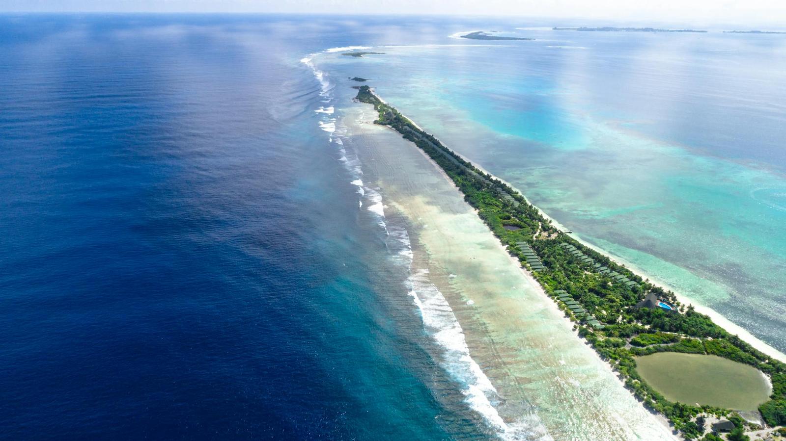 Aerial view of a narrow forested island bordered by breaking waves