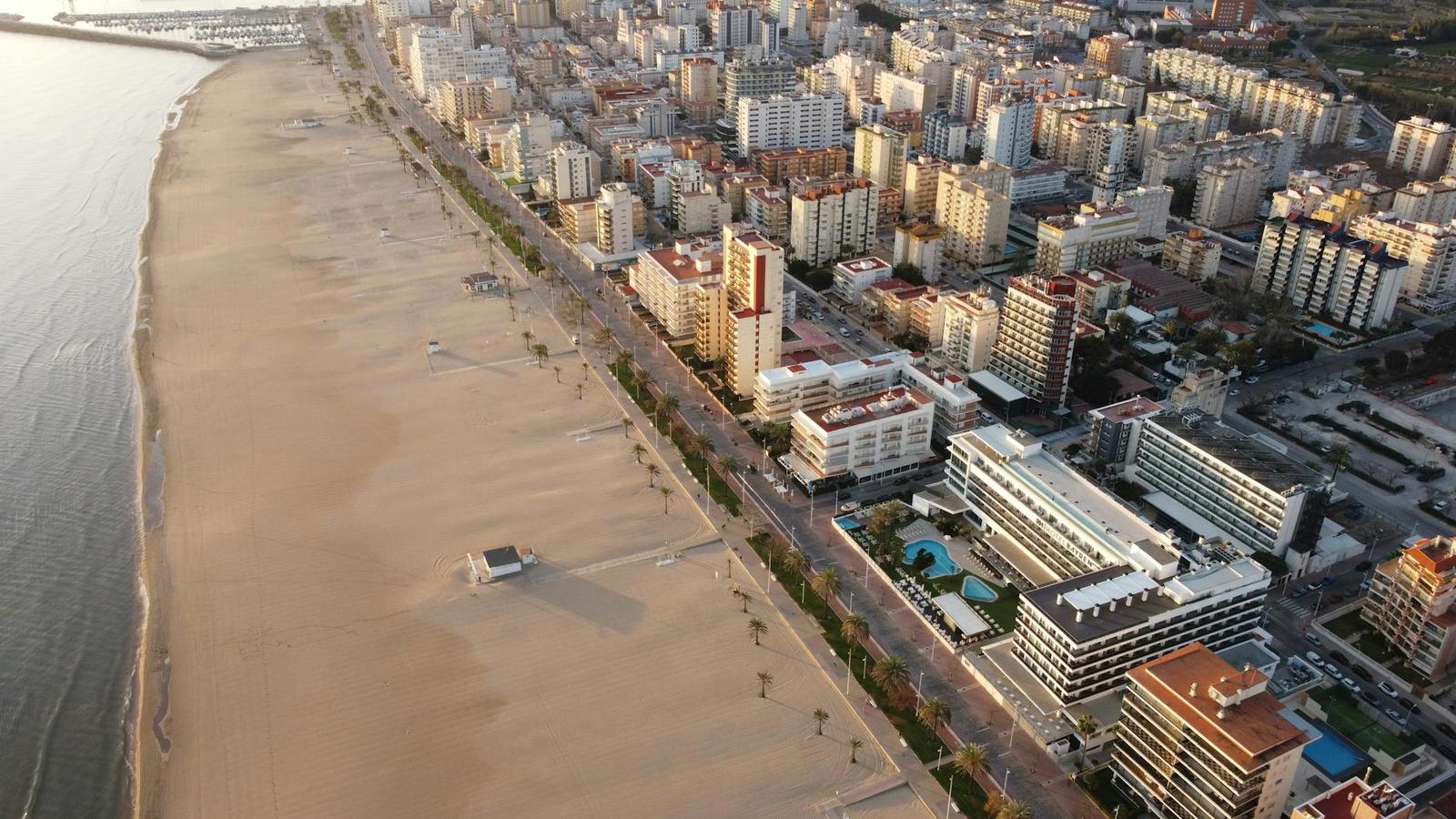 An aerial view of a long sandy beach lined with hotels and a promenade at sunset