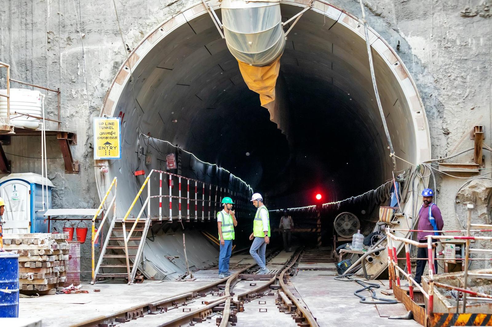 Workers in hi-vis vests inspecting rail tracks inside a tunnel under construction