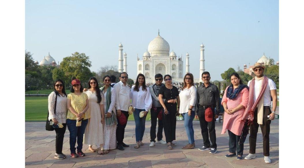 A group of people posing together in front of the Taj Mahal on a sunny day.