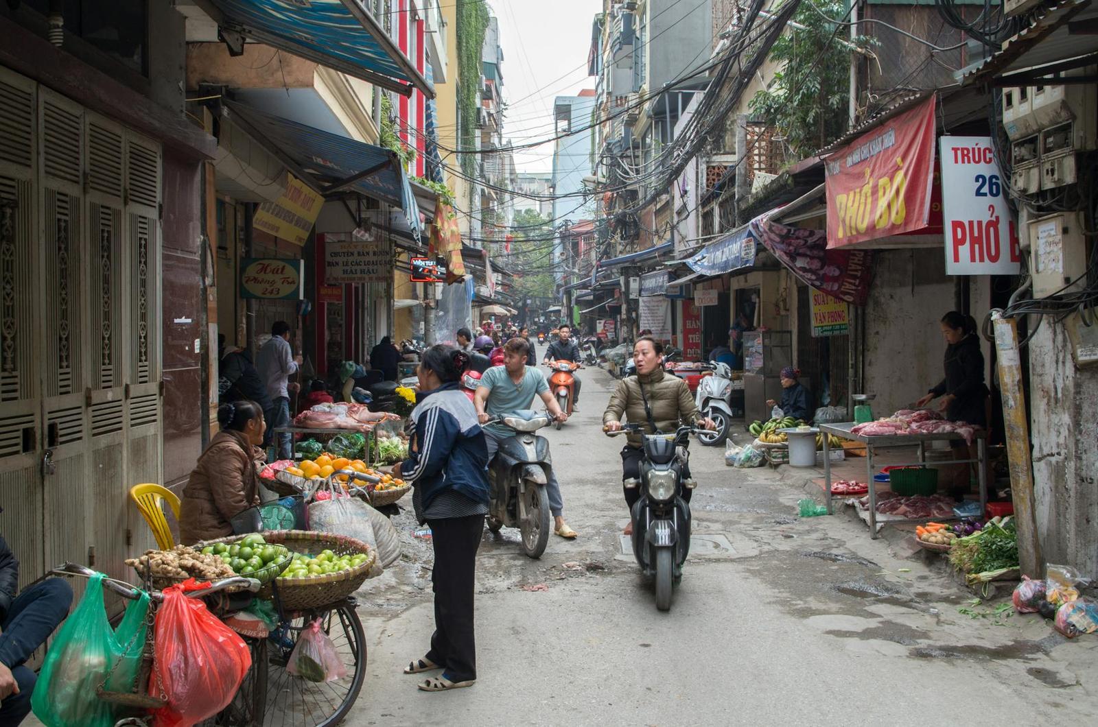 Busy market alley with motorbikes and vendors selling produce from street carts