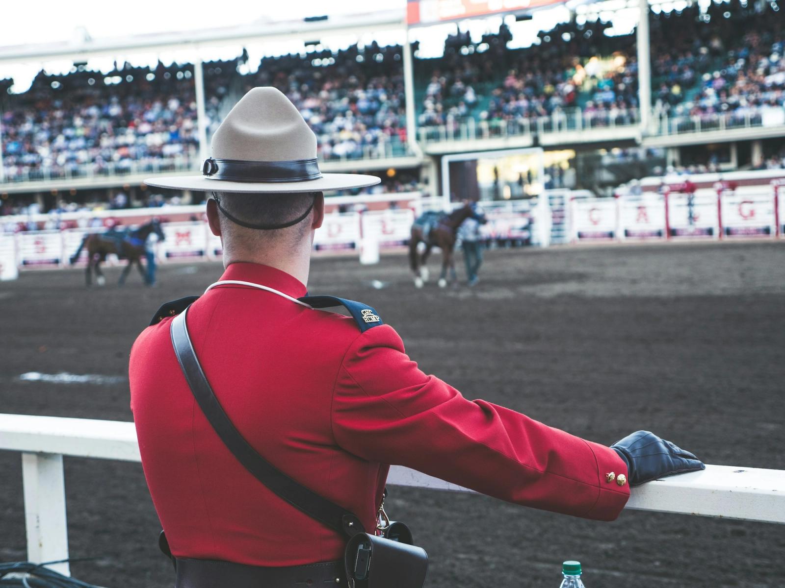 A Mountie in red dress uniform watching a rodeo from the rail