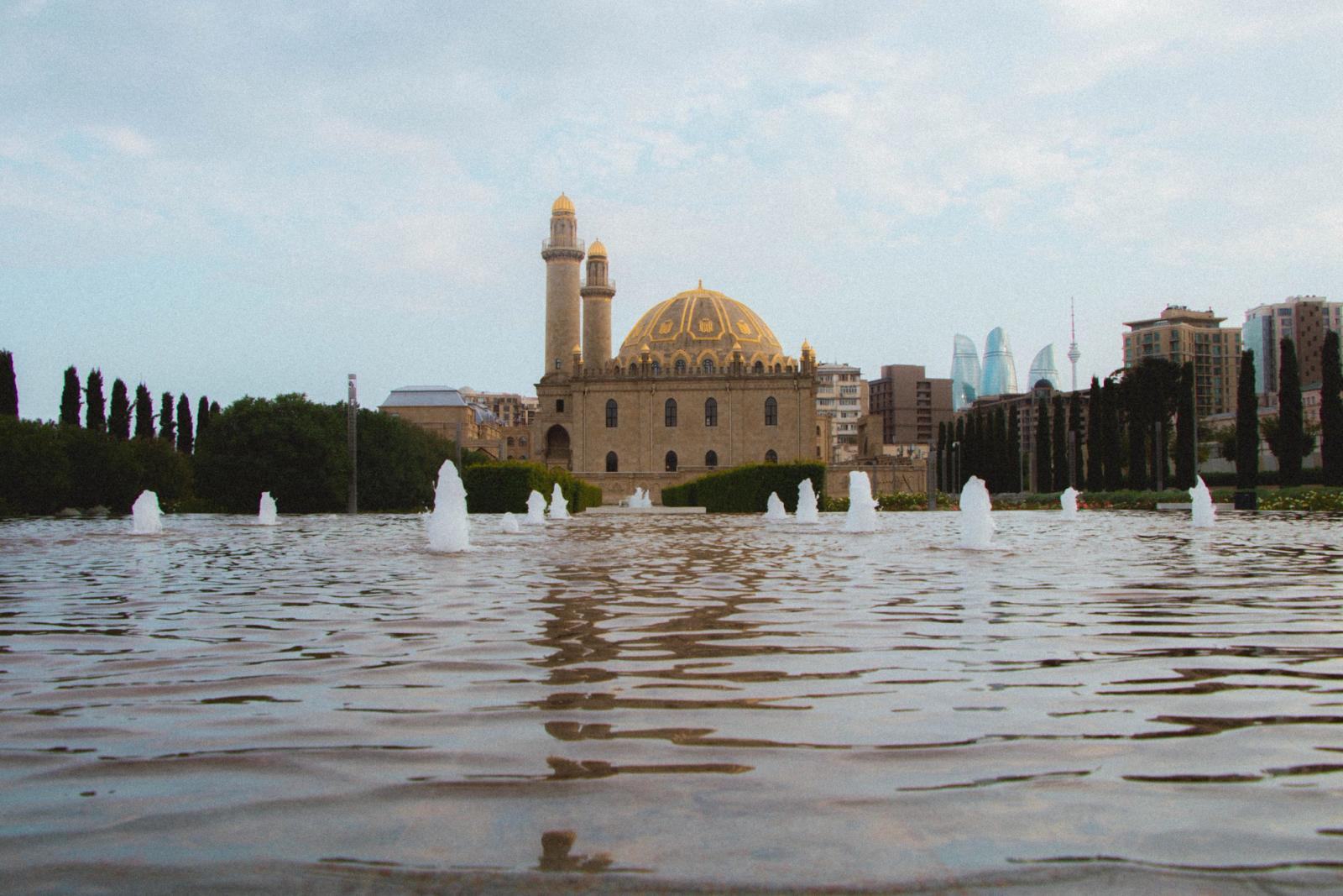 A stunning view of Baku's Taza Pir Mosque with fountain reflections and modern skyline in the background