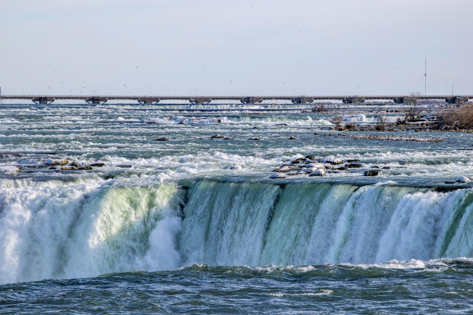 Wide waterfall cascading over rocks with a bridge in the distance