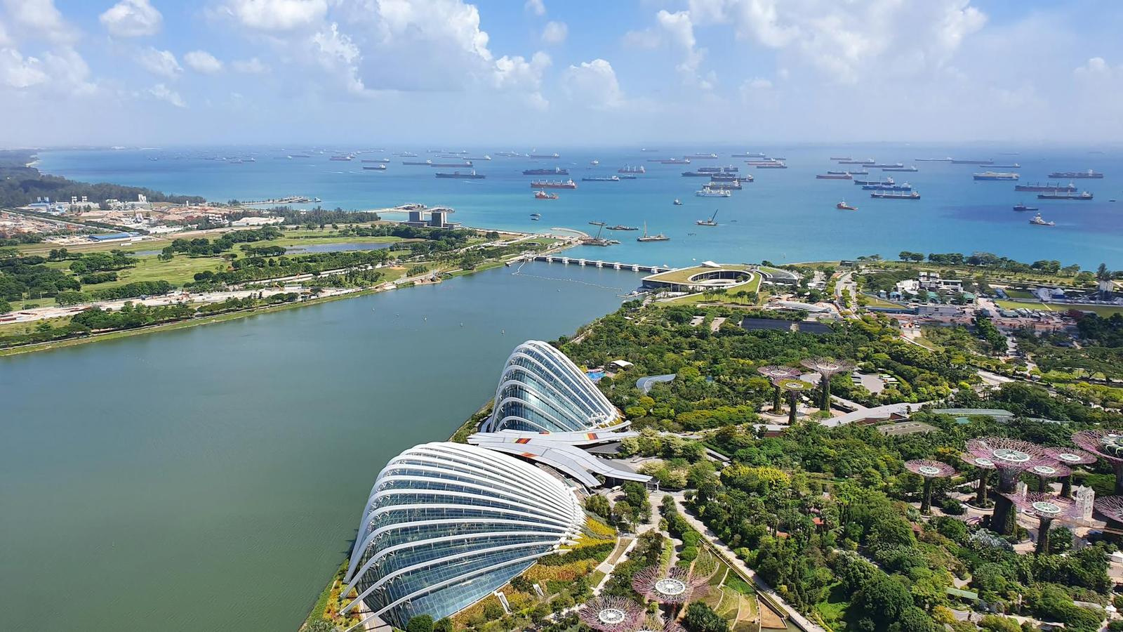 Aerial view of domed glasshouses beside a bay filled with anchored ships