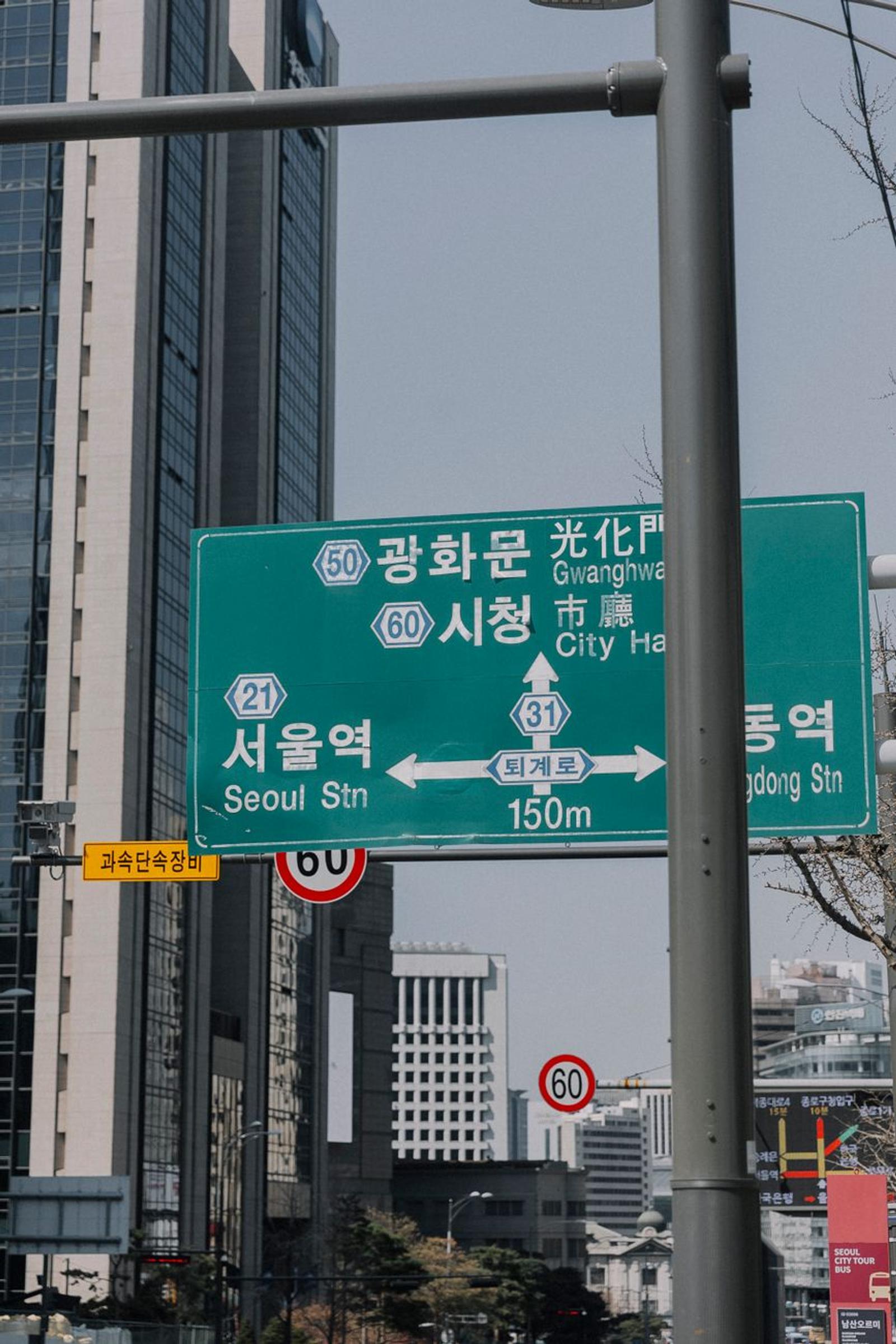 Korean directional street sign mounted against a city backdrop