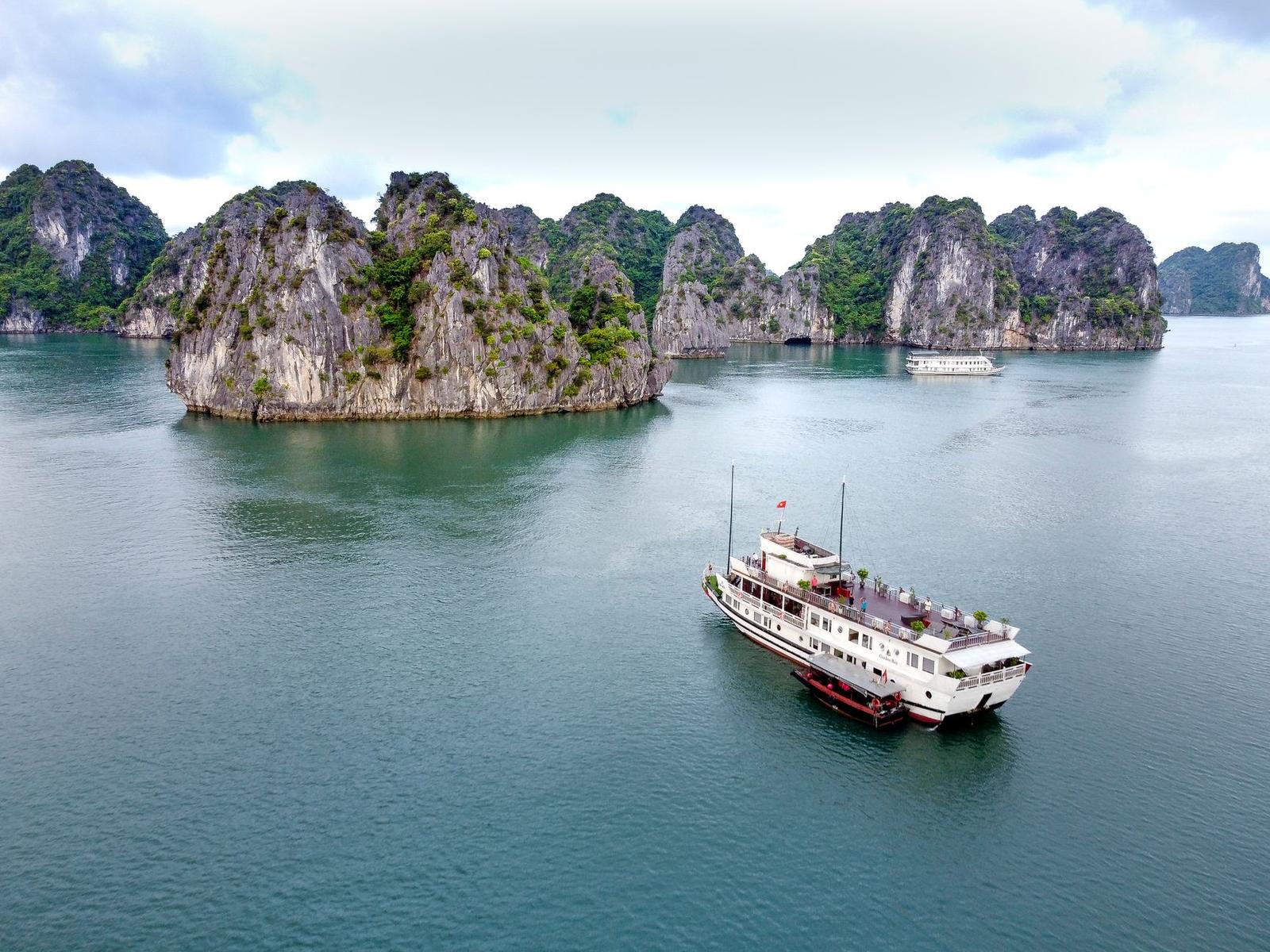 Height view of cruise vessel sailing in calm ocean to big rocks overgrown with green plants in daylight