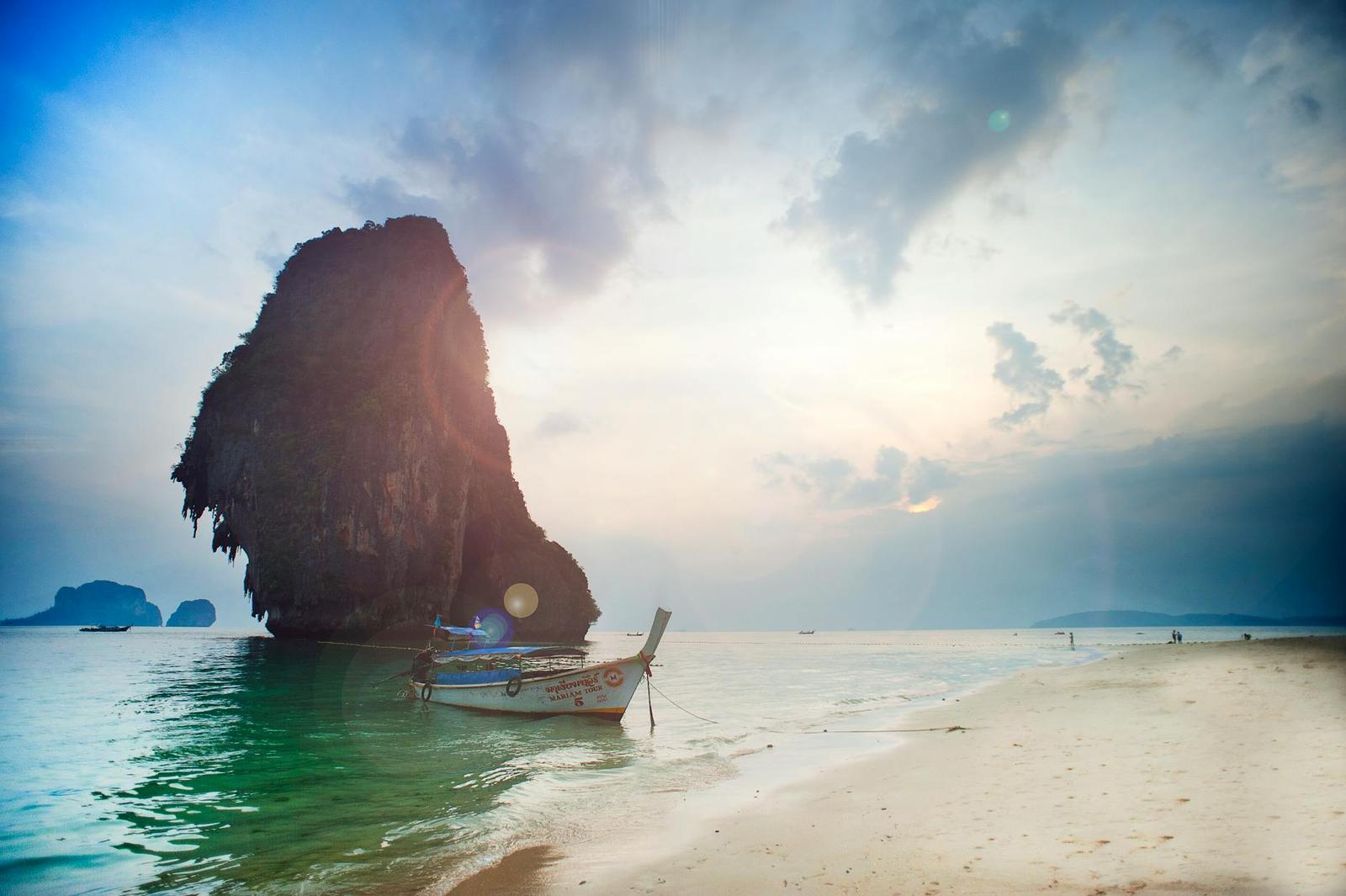 Longtail boat beside a tall rock outcrop on a beach at dusk