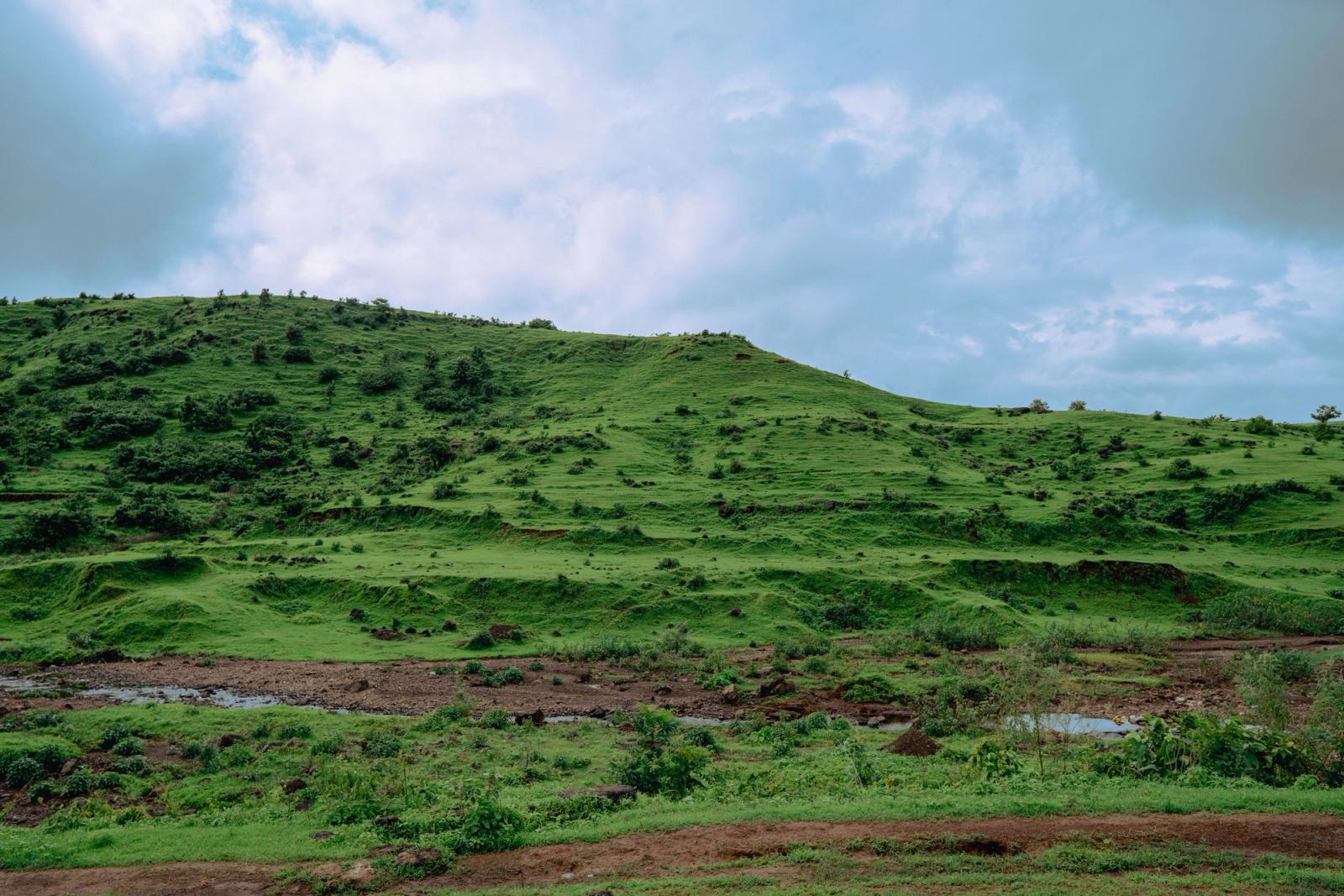Serene landscape of rolling green hills beneath a cloudy sky in Dhom, Maharashtra, India