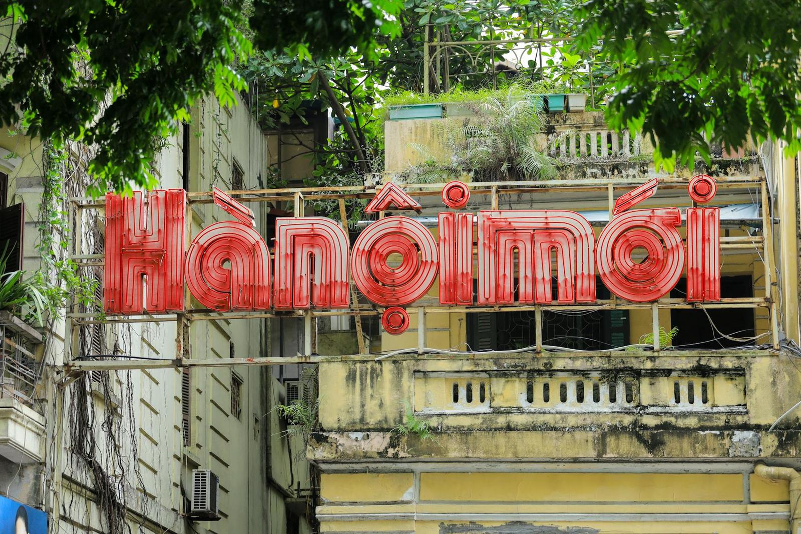 Vintage red neon shop sign mounted on a weathered building among tree branches