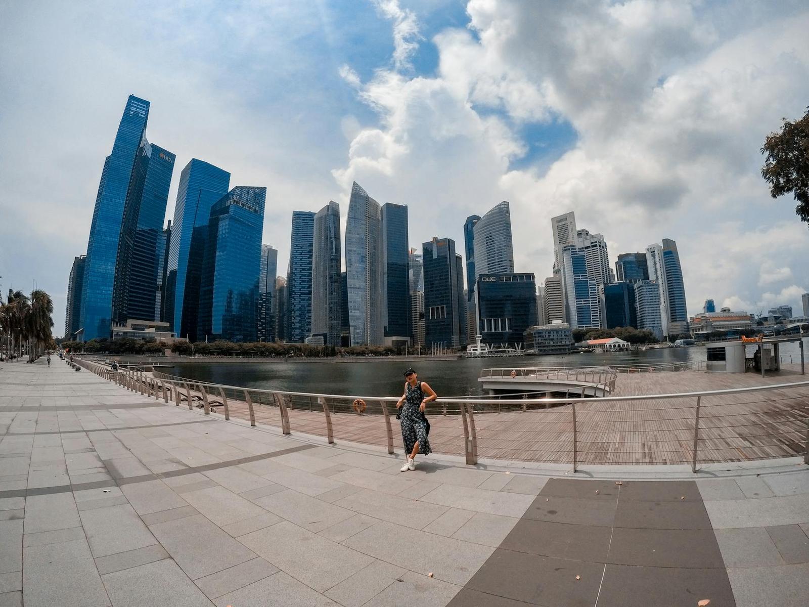 A waterfront promenade beside a glass skyscraper skyline under a partly cloudy sky