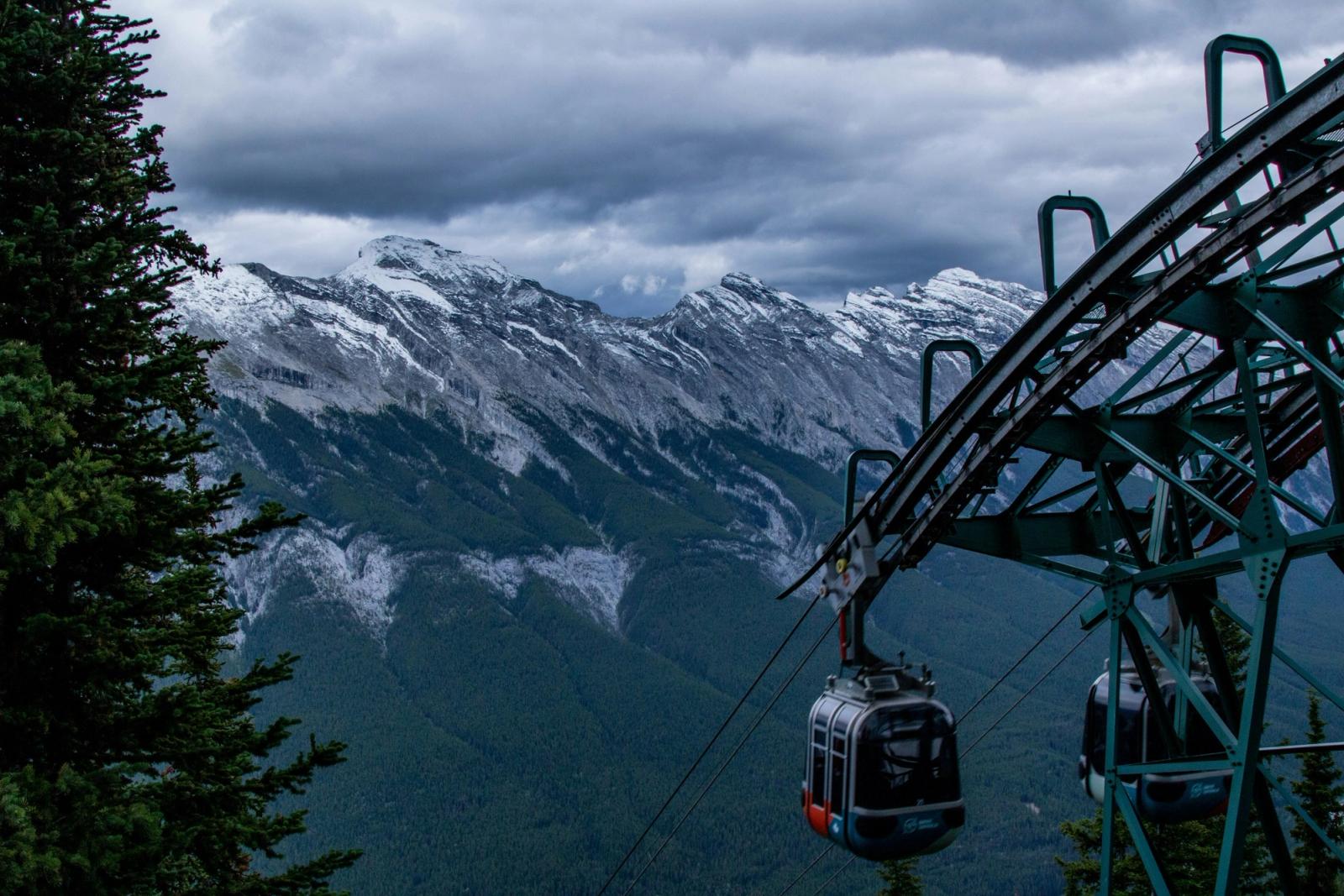 A cable car gondola climbing toward snow dusted mountain ridges under storm clouds