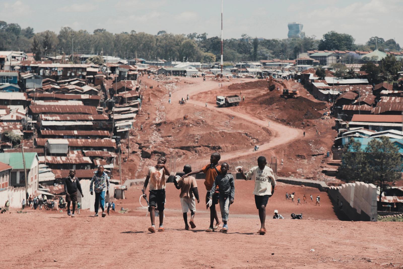 Group of teenagers walking in a suburban area with red soil paths and distant town view