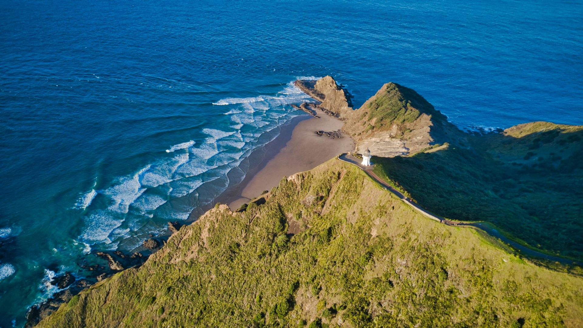 Aerial view of waves breaking on a sheltered beach below a green headland