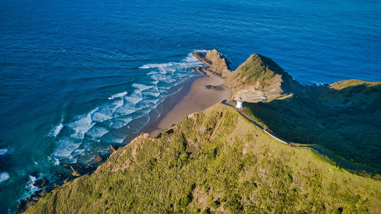 Aerial view of waves breaking on a sheltered beach below a green headland