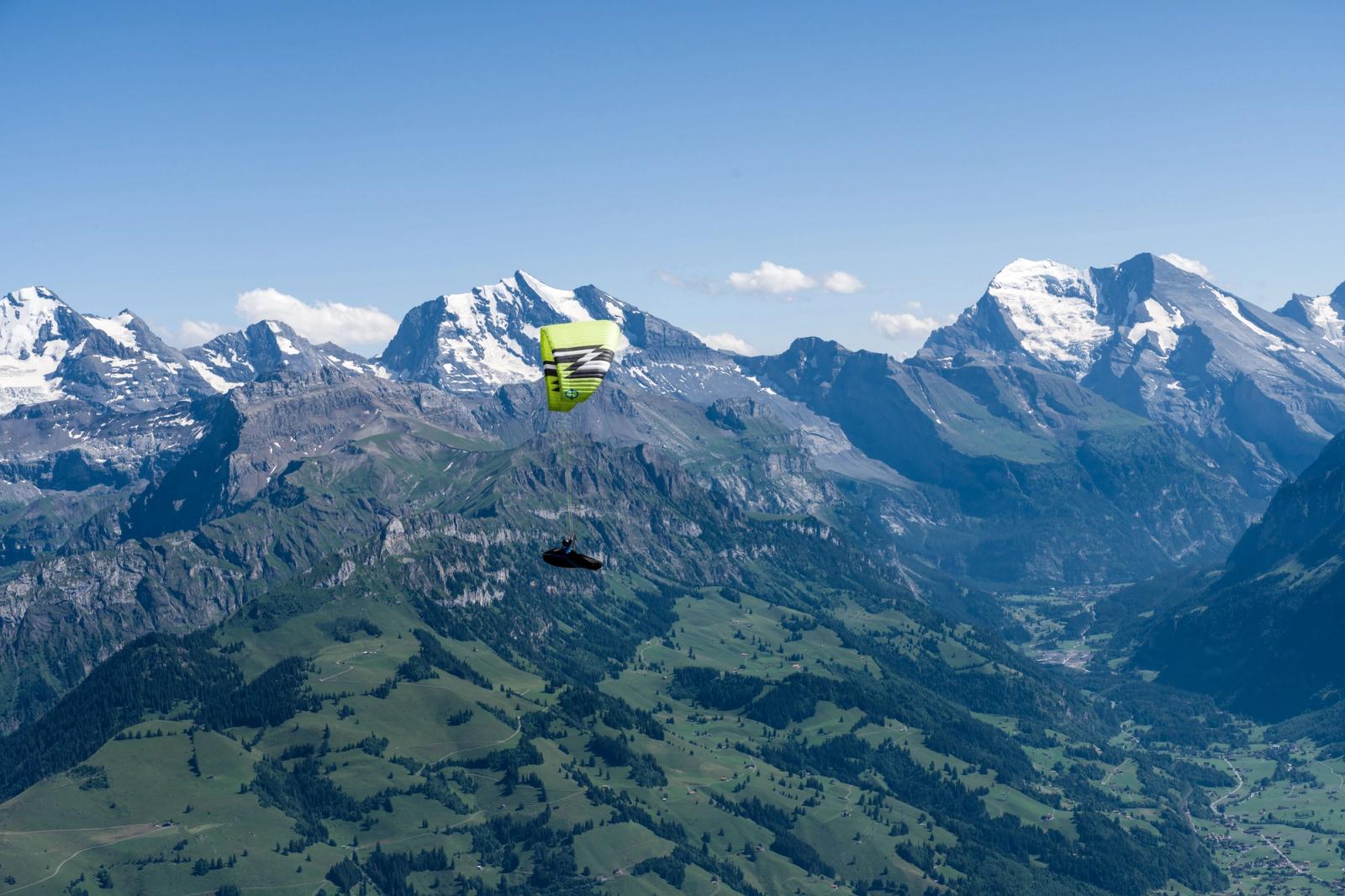 A paraglider soars above the majestic peaks of the Swiss Alps under a clear blue sky