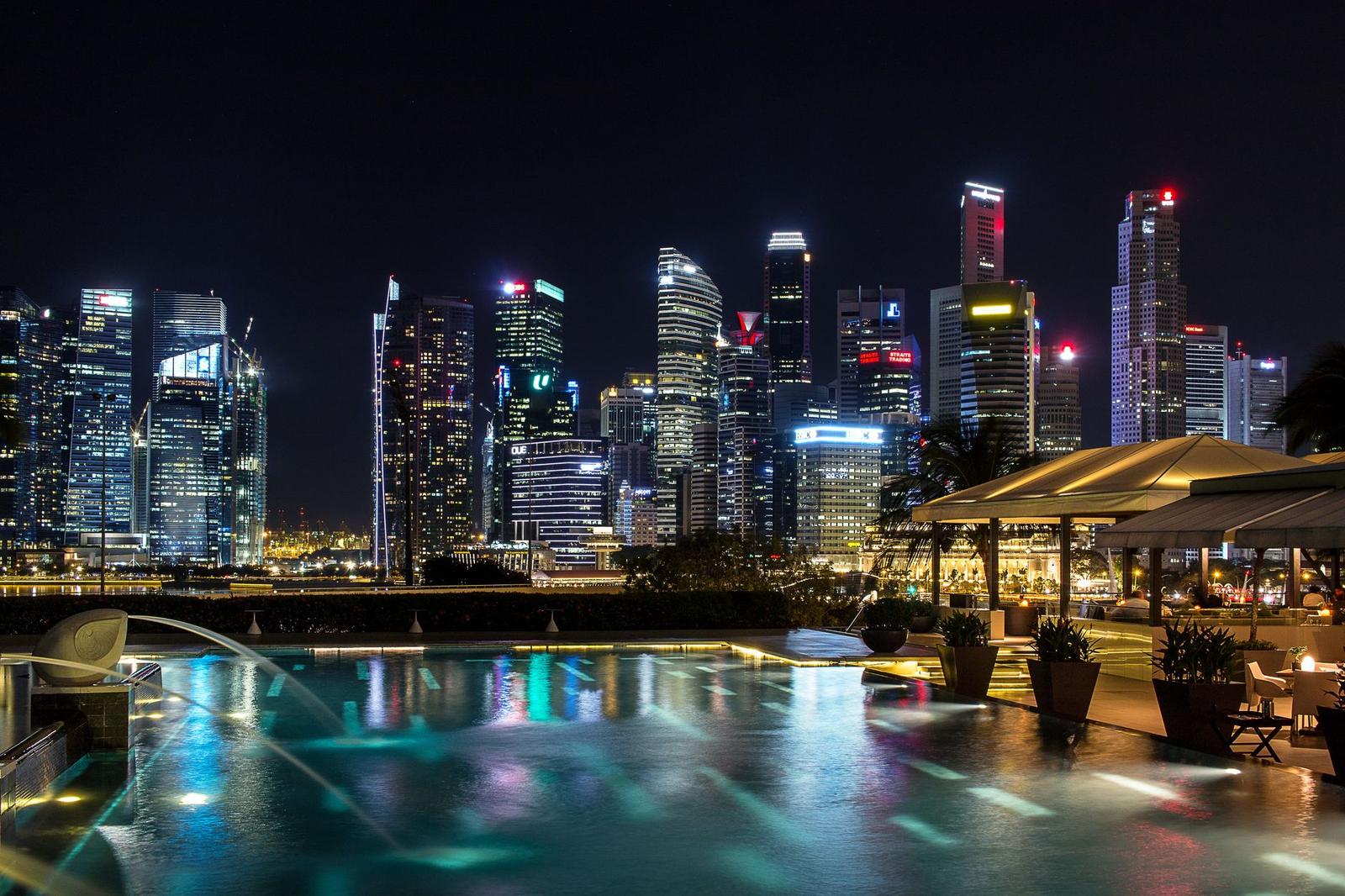 A rooftop infinity pool glowing at night above a dense city skyline