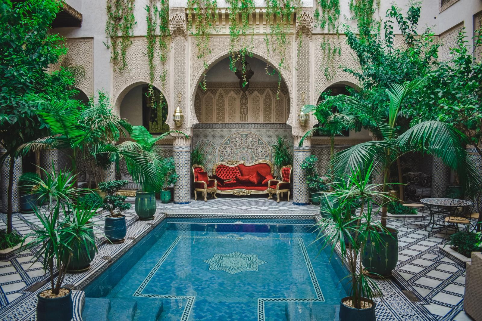 Elegant Moroccan courtyard featuring lush greenery and a decorative pool, perfect for a serene escape