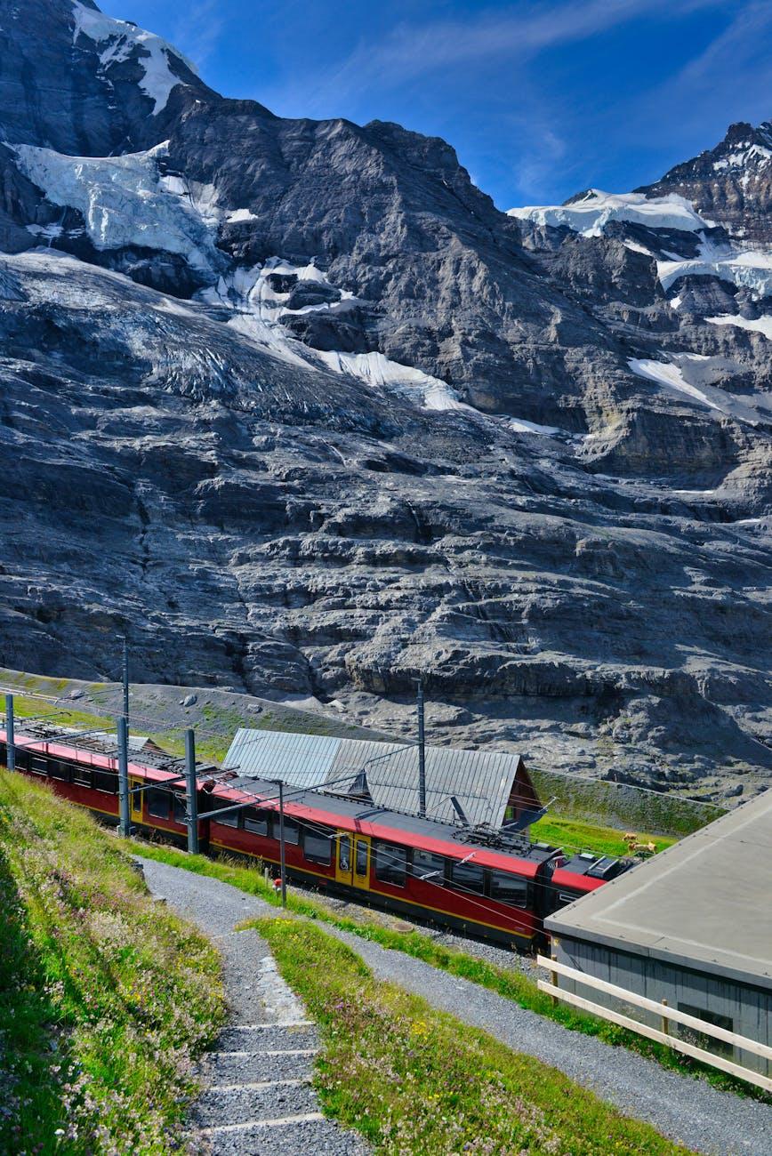 Red cogwheel train descending past a glacier-streaked mountainside