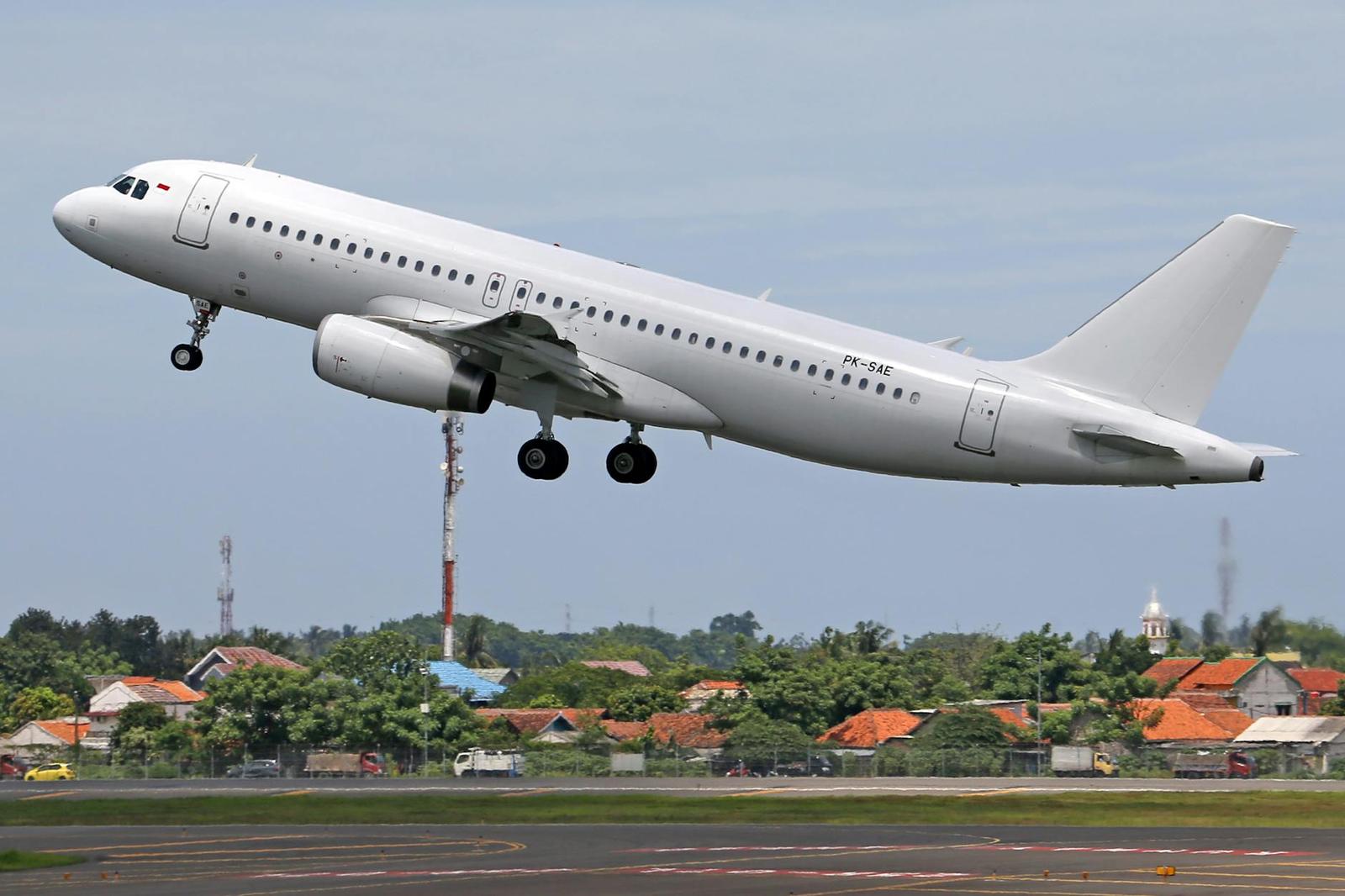 A white passenger jet climbs above a red-roofed town after takeoff