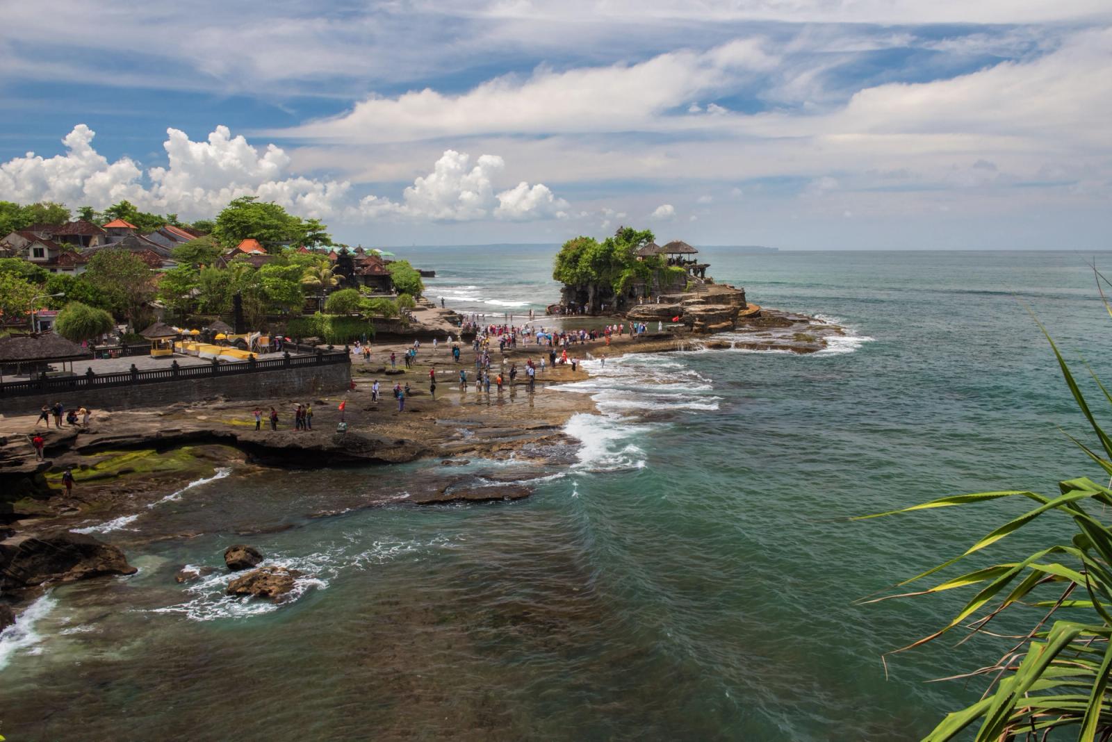 A breathtaking view of Tanah Lot Temple surrounded by the ocean in Bali, Indonesia with tourists exploring the area