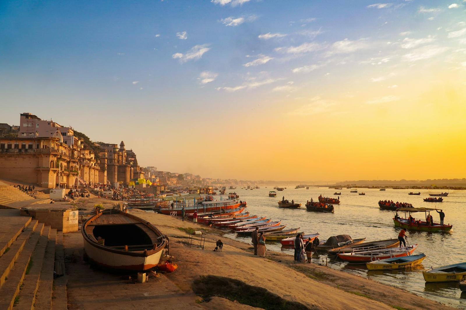 Boats gathered along a riverside ghat under a glowing sunset sky