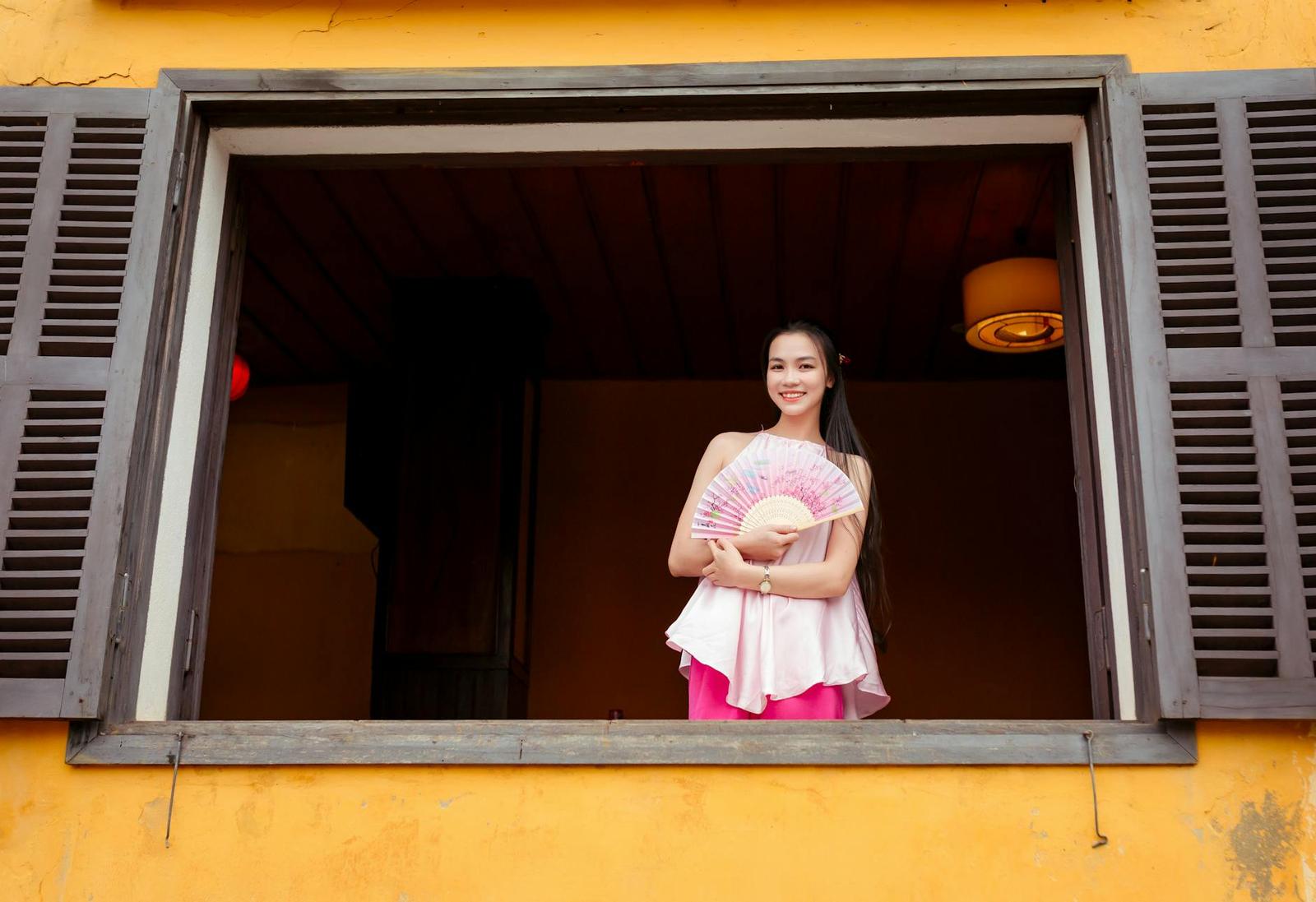 Close-up of a Vietnamese woman in traditional attire holding a fan in a window at Hội