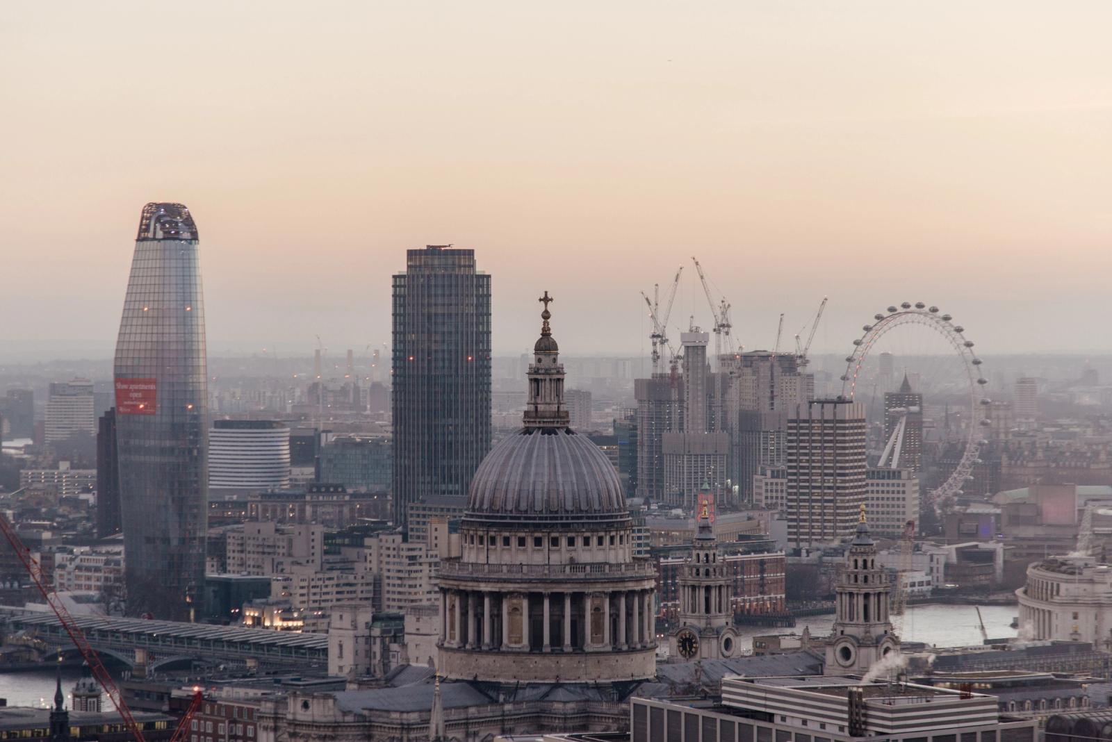 Cityscape of London with historic St Pauls cathedral with dome located near modern multistory skyscrapers and famous observation wheel near river