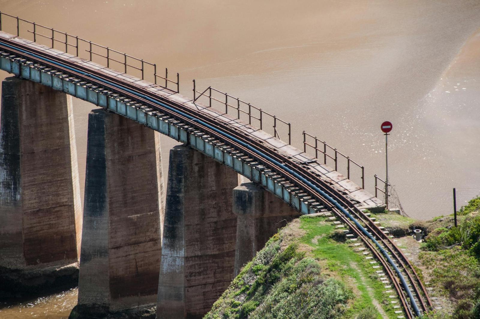 A curved railway trestle bridge arcing over a wide muddy river