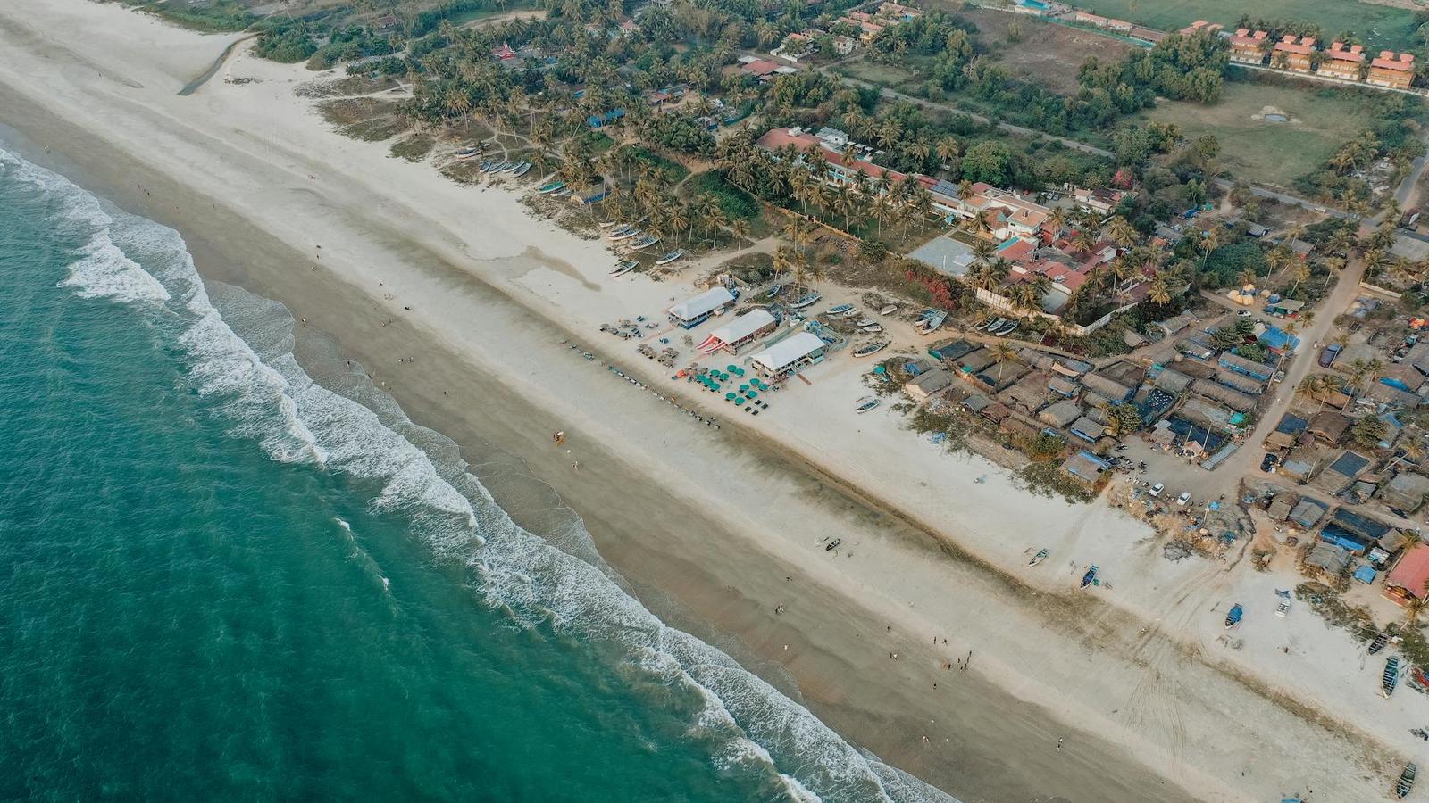 Aerial view of a sandy beach town where waves meet a dense cluster of buildings