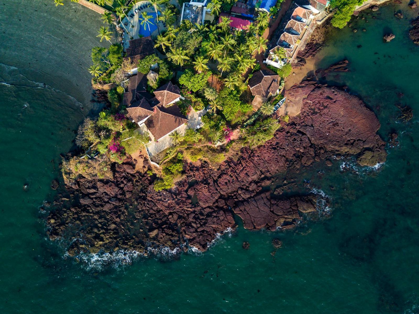 Aerial view of a rocky headland with villas among palm trees