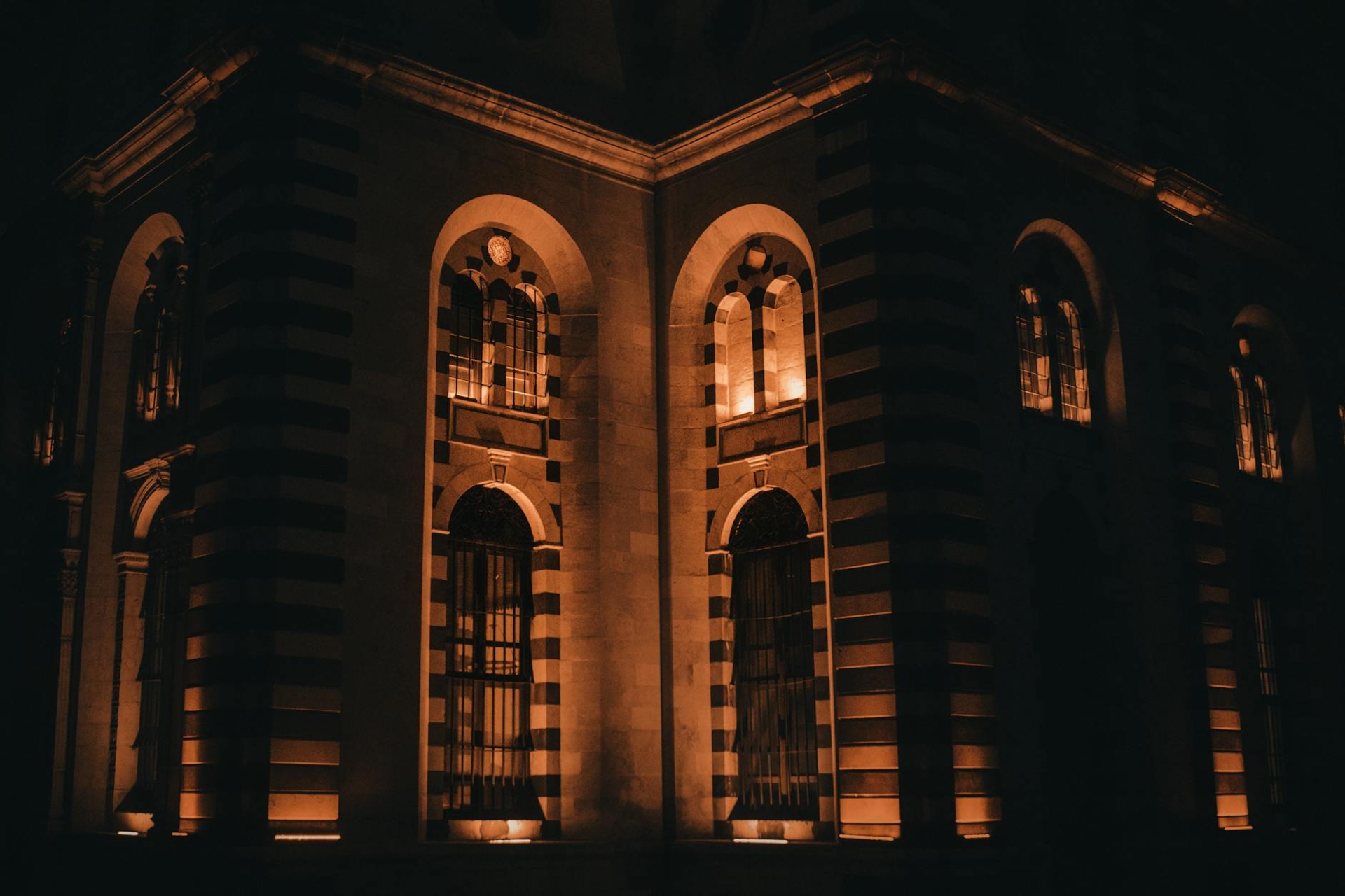 An arched stone building facade lit warm orange at night