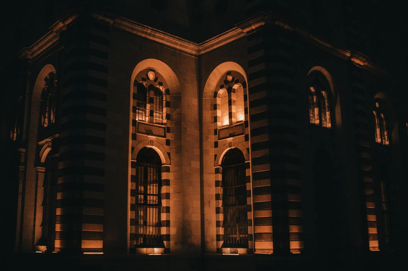 An arched stone building facade lit warm orange at night