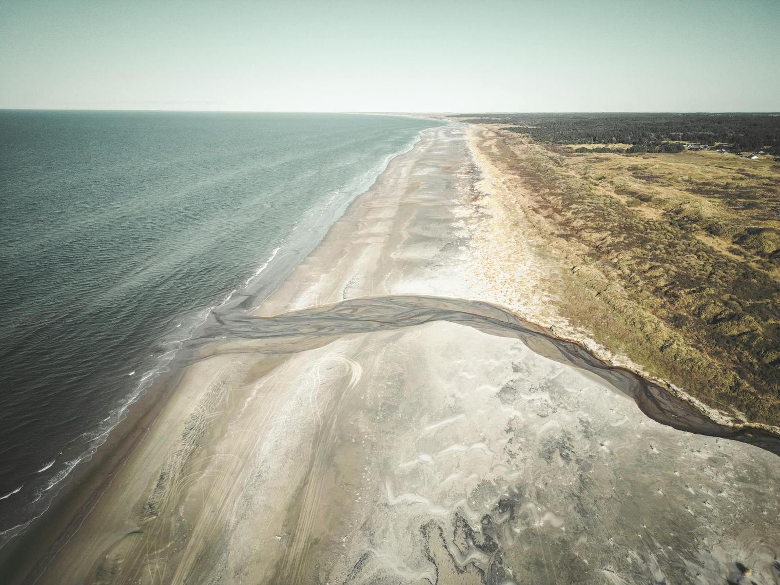 Aerial view of a tidal channel cutting through a long sandy beach