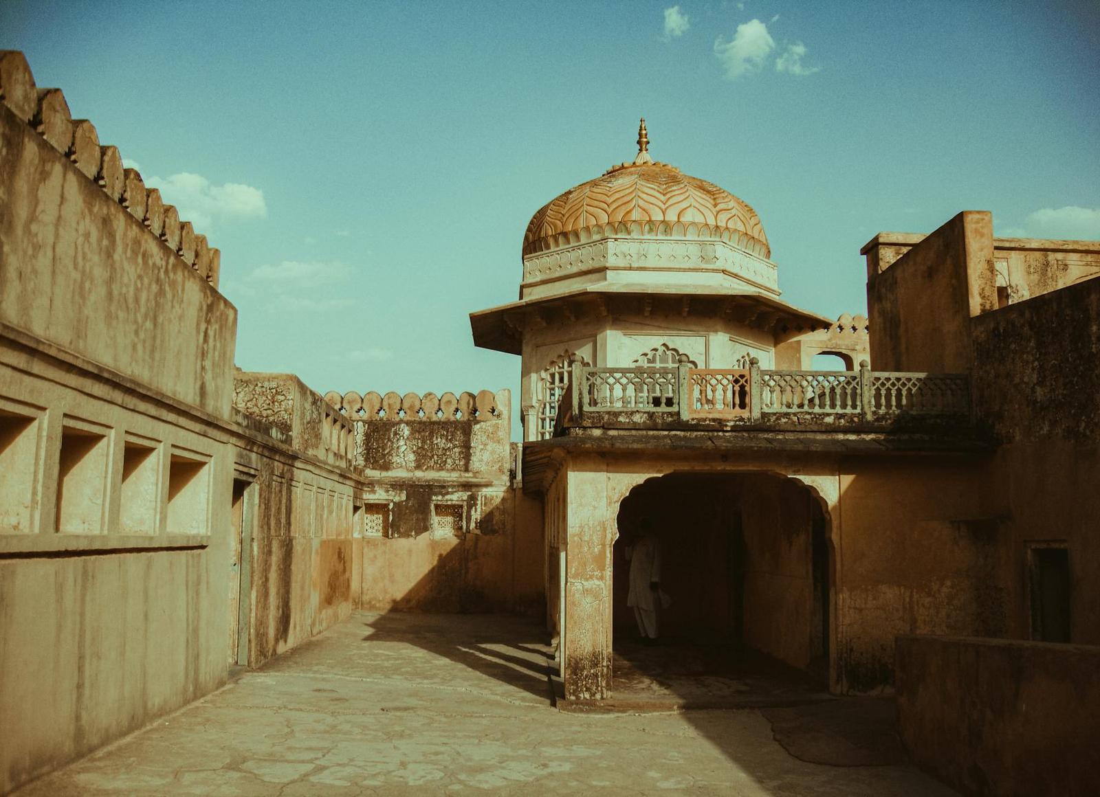 A domed chhatri pavilion beside an archway in a sandstone courtyard