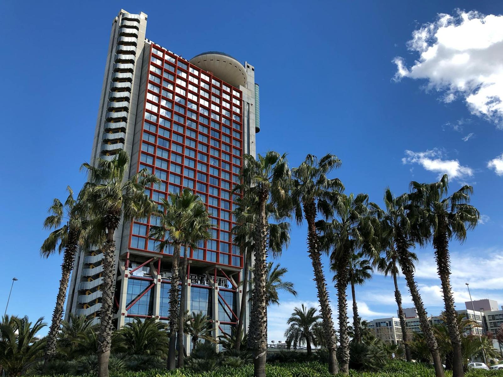 Tall red and white hotel tower rising behind a row of palm trees