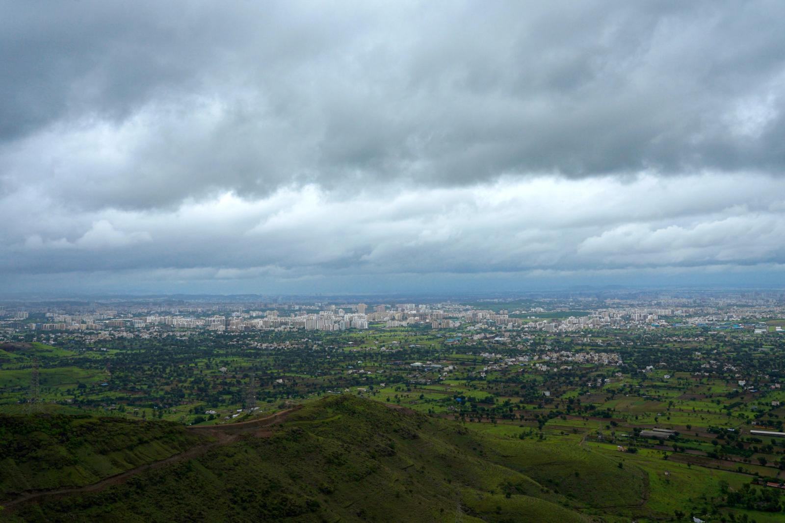 Aerial panorama of Holkarwadi, India featuring lush fields and urban landscape beneath a cloudy sky