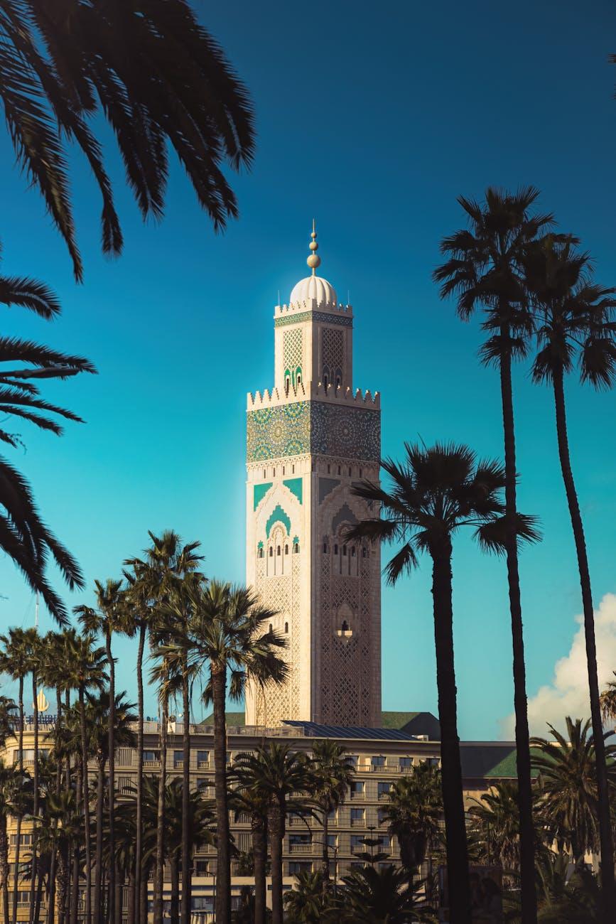 Tiled minaret tower rising above palm trees against a bright blue sky