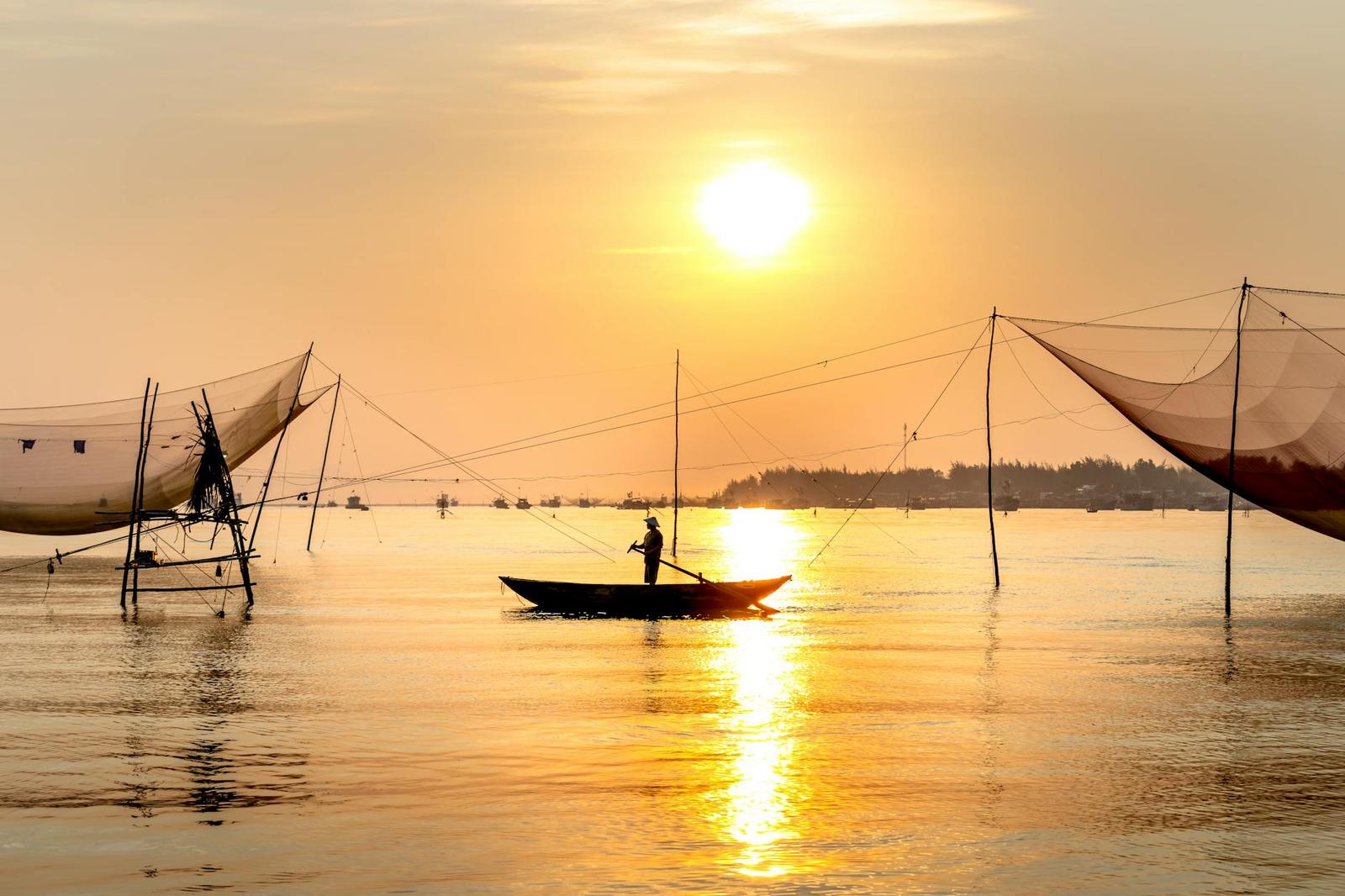Silhouette of a fisherman poling his boat among tall net frames at sunrise