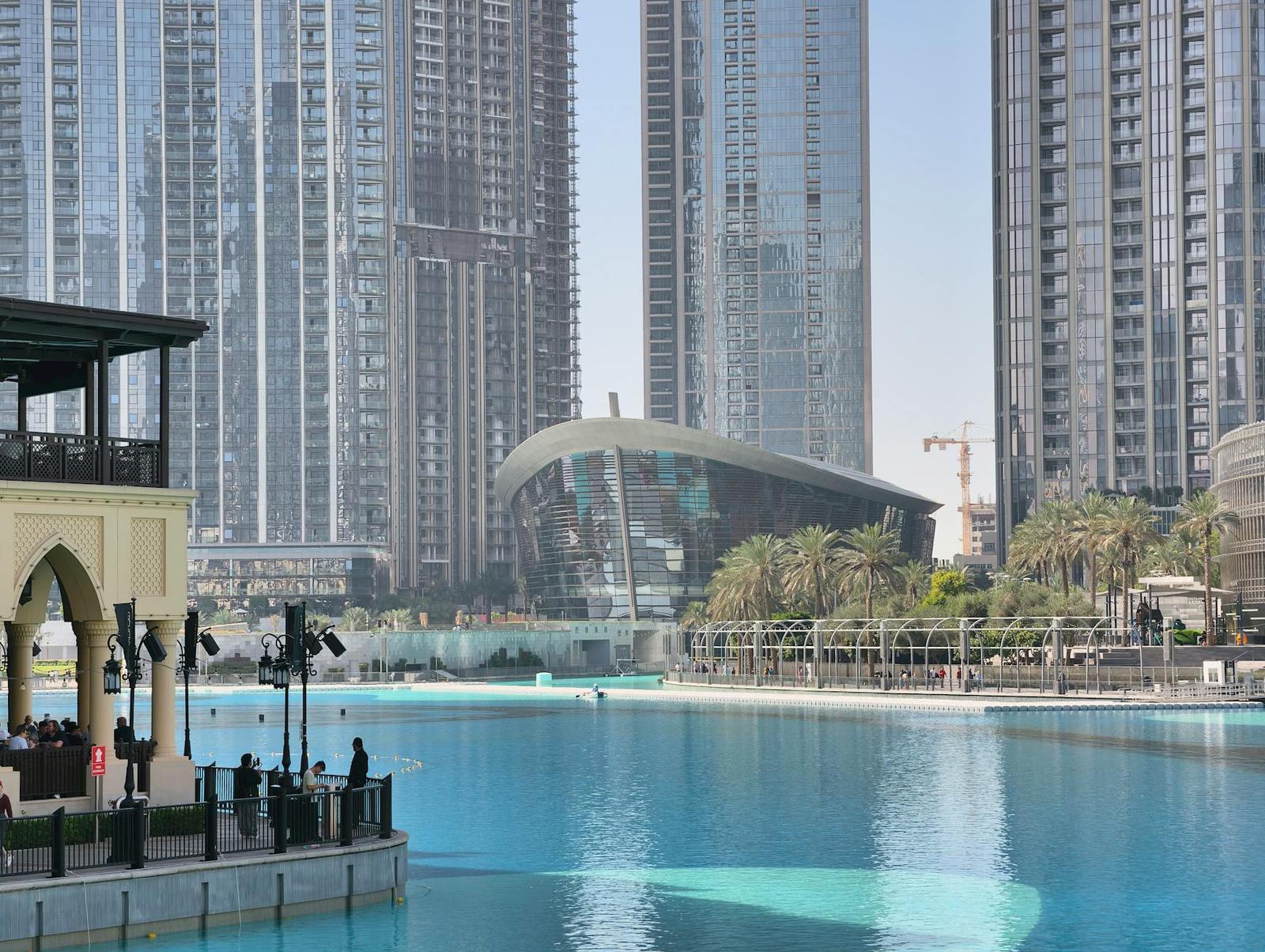 A turquoise canal beside modern skyscrapers with a curved glass building in the distance
