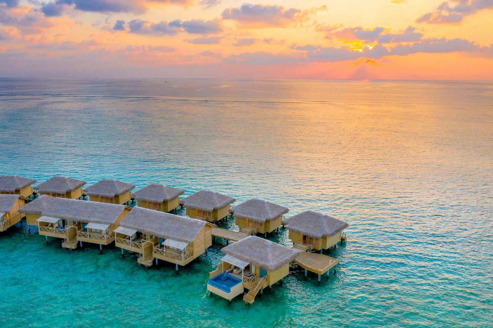 Overwater bungalows on stilts silhouetted against a pastel sunset sea