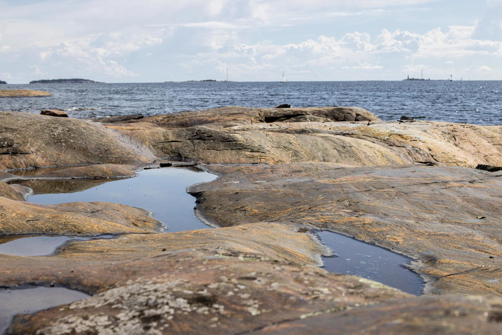 Scenic view of a rocky coastline in Helsinki with distant islands in the background