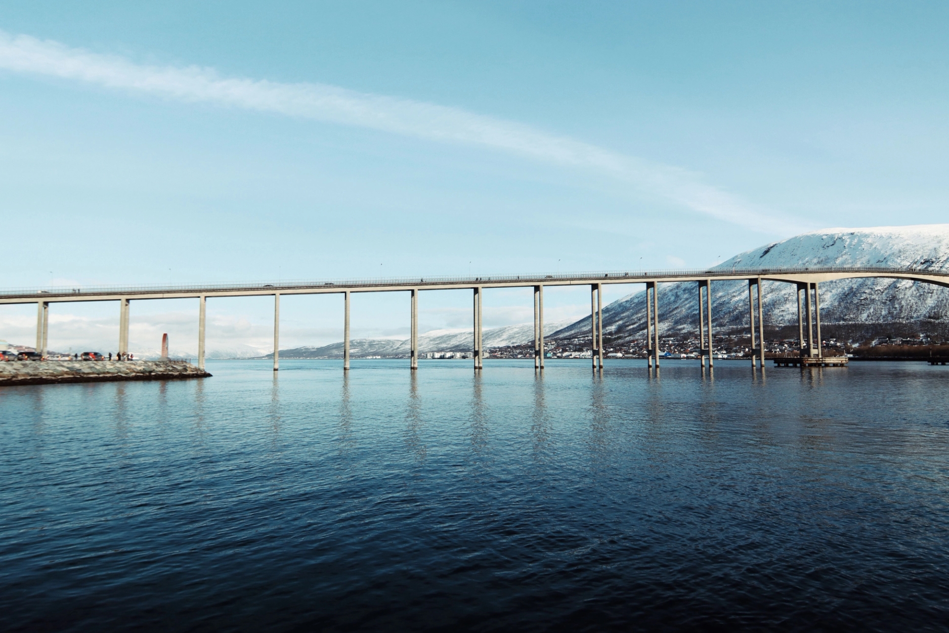Scenic view of Tromsø Bridge spanning the Arctic waters against a snowy mountain backdrop
